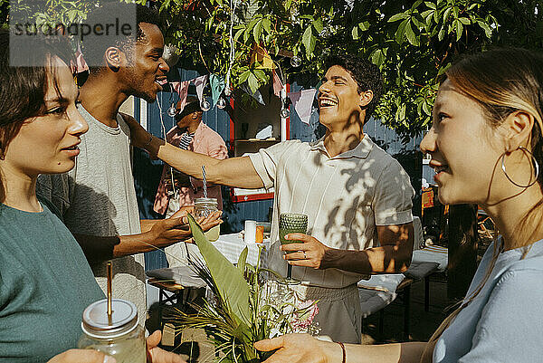 Happy multiracial male and female friends talking with each other while enjoying drinks at party