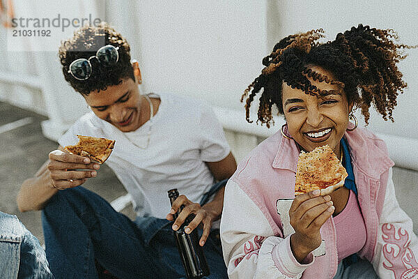 High angle view of curly hair woman eating pizza with male friend while sitting at parking lot