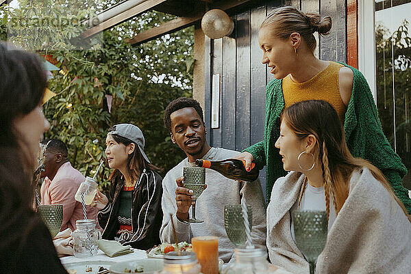 Woman serving drink to male friend sitting at dining table in back yard