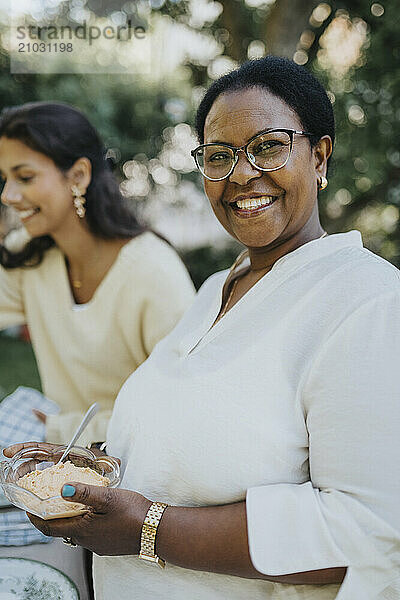 Portrait of cheerful senior woman holding ice cream bowl while standing at back yard