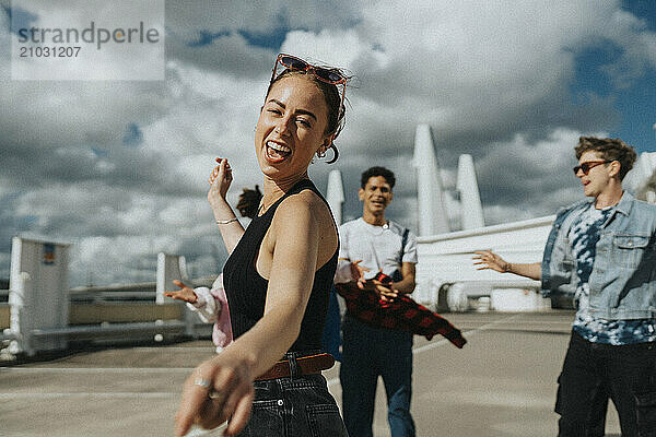 Side view portrait of young woman dancing with friends at parking lot under cloudy sky