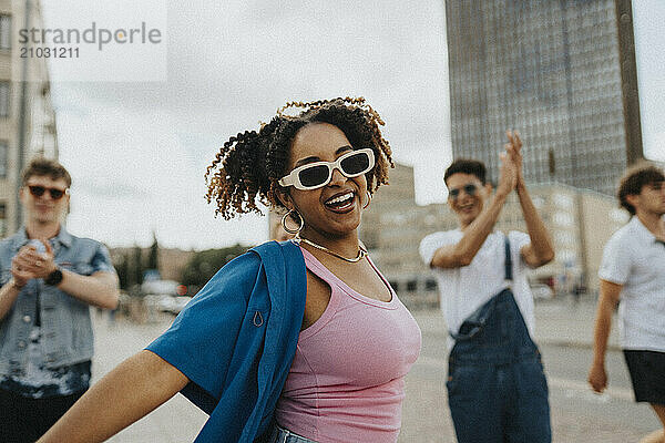 Portrait of cheerful curly hair woman in sunglasses dancing on street