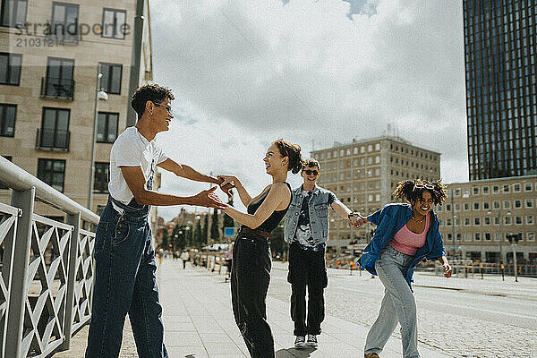 Carefree young male and female friends dancing and having fun while walking on street under cloudy sky