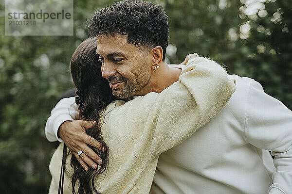 Smiling man hugging teenage family friend in back yard