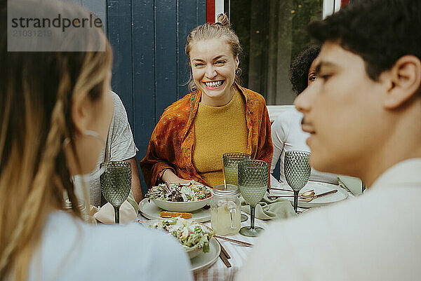 Smiling woman looking at friends talking with each other while enjoying at dinner party