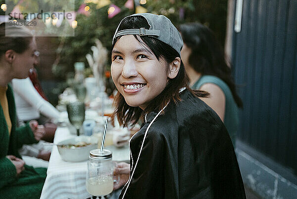 Portrait of smiling young woman wearing cap and sitting with friends at party in back yard