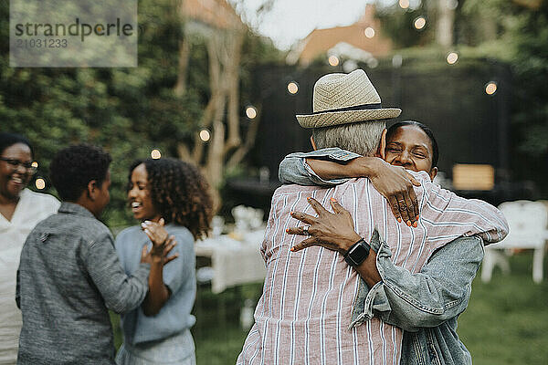 Happy woman greeting senior man during social gathering at garden party