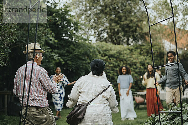 Cheerful male and female family members welcoming grandparents during social gathering at garden party