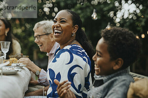 Cheerful mid adult woman having fun with male family members at lunch party