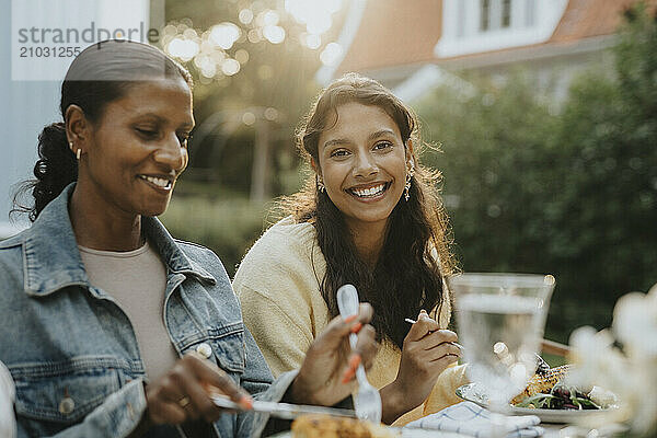 Portrait of cheerful teenage girl having lunch with mother at garden party