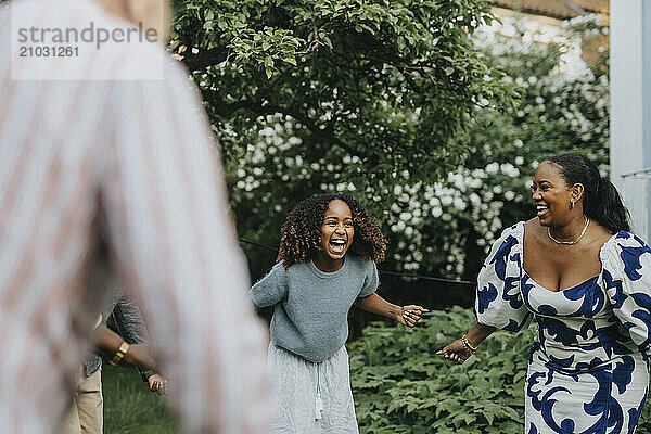 Cheerful mother and daughter dancing with family members in back yard