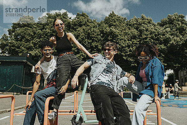 Happy young male and female friends enjoying and sitting on metal bars at playground