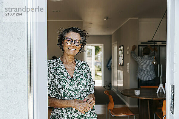 Portrait of happy senior woman standing near doorway of house