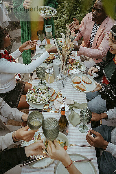 High angle view of friends toasting drinks while celebrating at dinner party in back yard