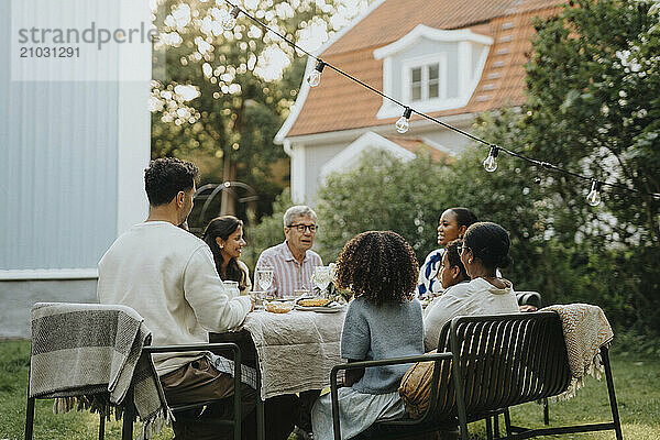 Male and female family members discussing and having lunch during social gathering at garden party