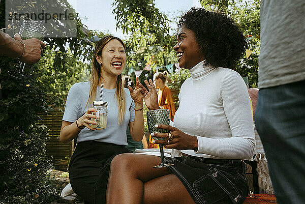 Cheerful female friends talking with each other while enjoying drinks at dinner party