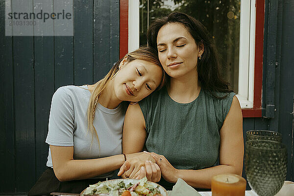 Smiling woman holding hands of female friend sitting at party in back yard