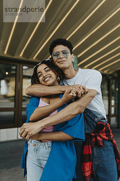 Portrait of fashionable young man with arm around female friend standing and holding hands outside store