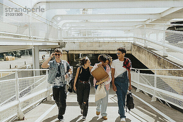 Fashionable young male and female friends talking and walking on footpath of parking garage at sunny day