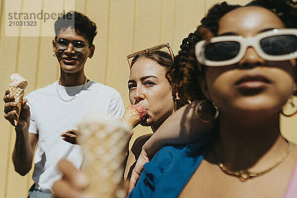 Young woman eating ice cream with male and female friends against corrugated wall