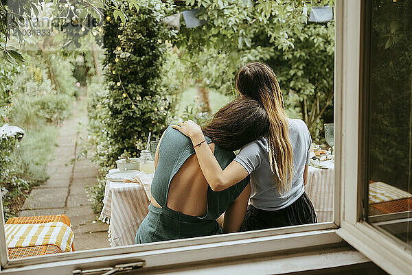 Woman with arm around female friend sitting near window