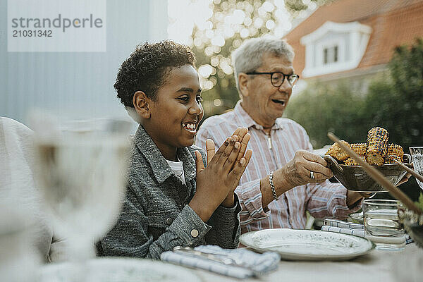 Excited boy clapping while having lunch with grandfather at garden party