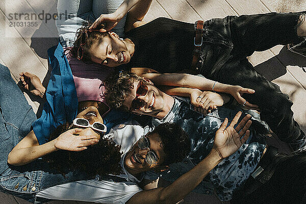 Directly above shot of cheerful young male and female friends lying down on floor in sunlight