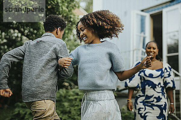 Carefree sister dancing arm in arm with brother during garden party