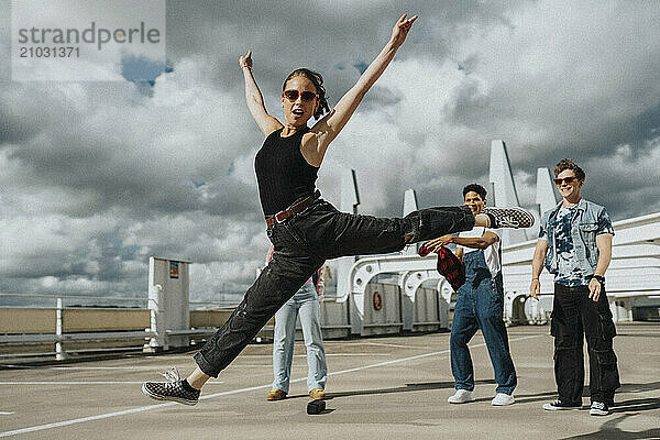 Portrait of young woman in casuals doing split in parking lot under cloudy sky