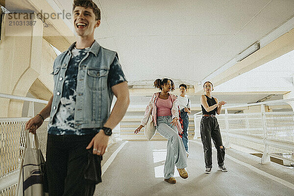 Carefree young male and female friends dancing while walking on footpath of parking garage