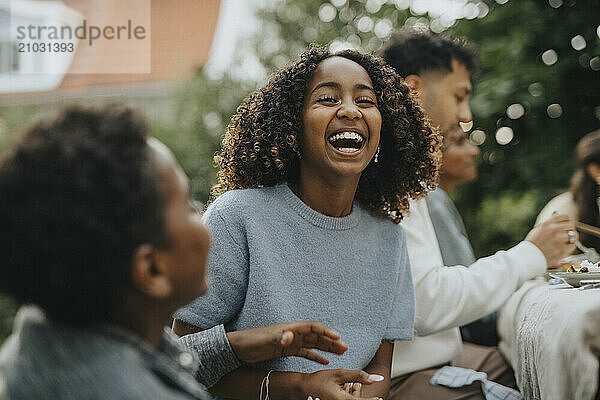 Portrait of cheerful curly hair girl having fun with brother during social gathering in back yard