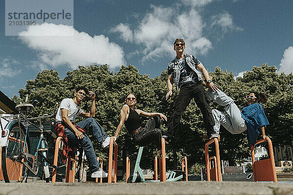 Low angle portrait of young male and female friends enjoying on metal bars at playground