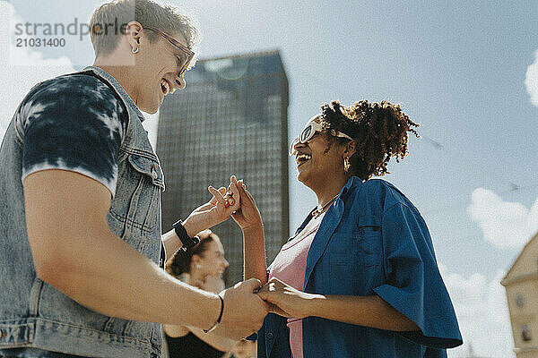 Low angle view of cheerful young fashionable woman dancing with male friend under sky