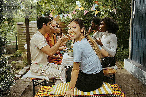 Portrait of smiling woman looking over shoulder while sitting with friends at dining table during party