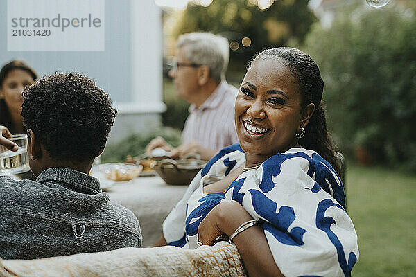 Portrait of happy mid adult woman looking over shoulder while sitting at social gathering in back yard