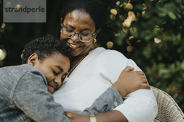 Curly hair boy embracing grandmother sitting at back yard