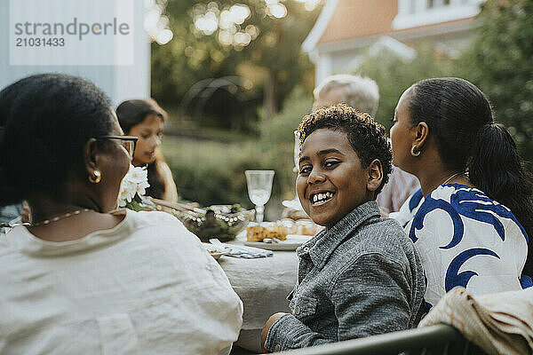 Portrait of playful boy looking over shoulder while sitting with family members at dinner party