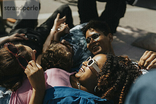 Happy fashionable young woman lying down on floor with male and female friends in sunlight