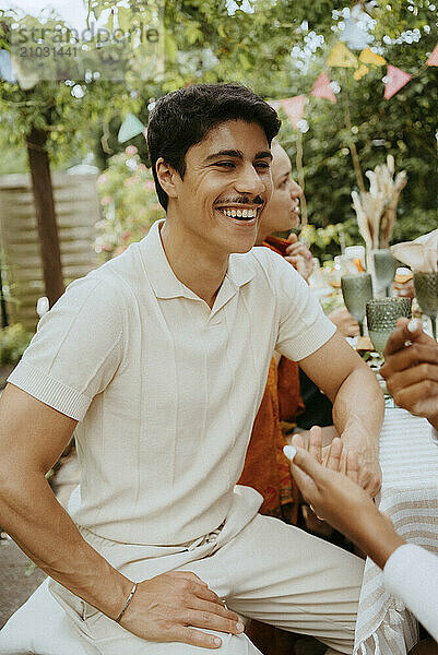 Happy young man talking with friends while sitting at dining table during dinner party