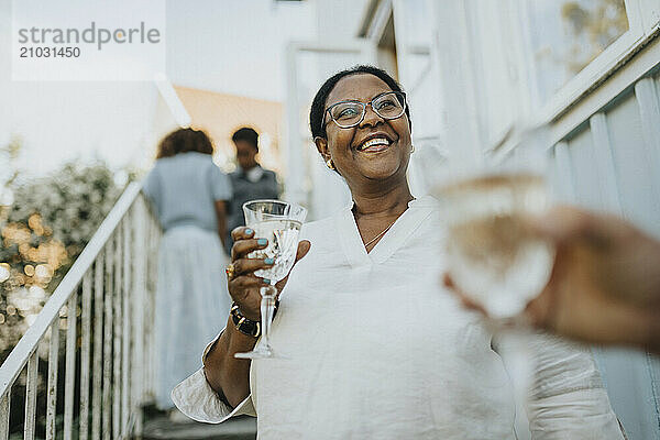 Low angle view of happy senior woman holding glass and standing on staircase outside house