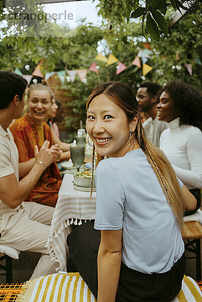 Smiling woman looking over shoulder while sitting with friends at dining table during party