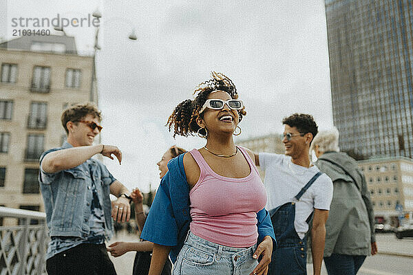 Happy fashionable young curly hair woman in sunglasses enjoying with male and female friends at street