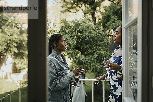 Mature woman discussing with female friend and standing in balcony at garden party