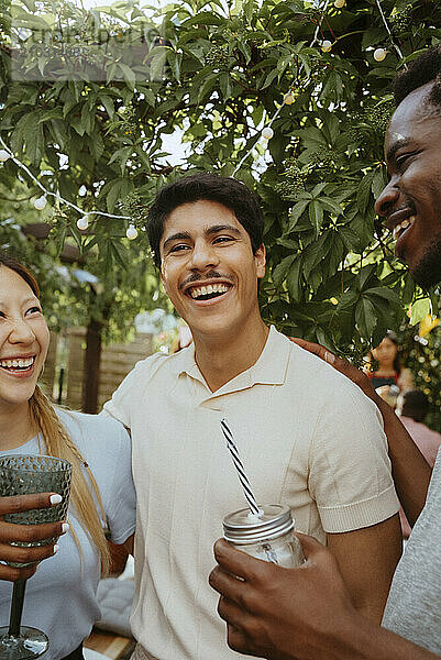 Happy young man with friends enjoying drinks in back yard during dinner party