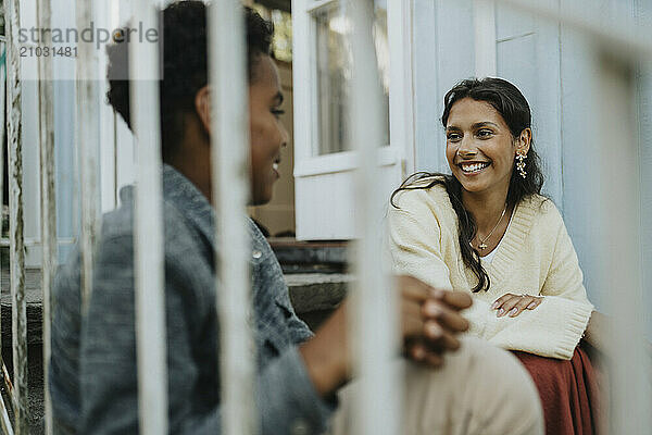 Happy teenage girl talking with male cousin and sitting on steps outside house