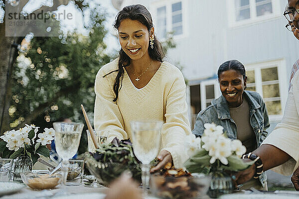 Happy teenage girl setting table for lunch with family members at garden party