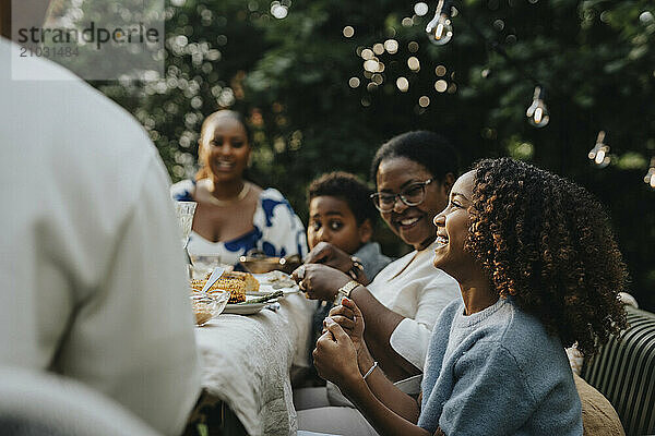 Cheerful girl discussing and having fun with family members at lunch during social gathering