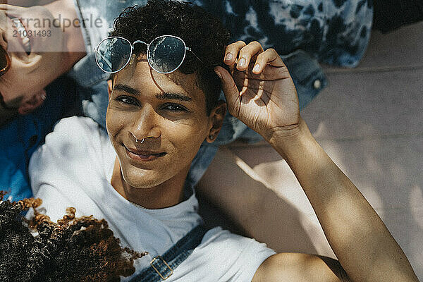 Portrait of hipster young man holding sunglasses and lying down on floor with friends in sunlight