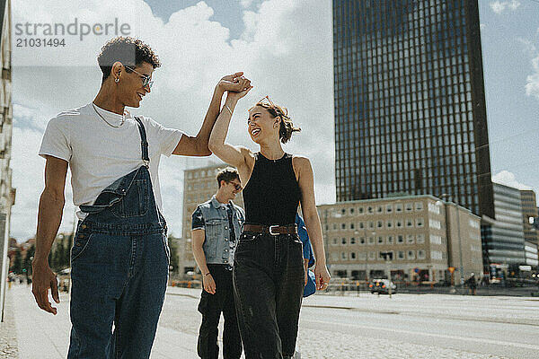 Fashionable young man dancing with female friend while walking on street in city