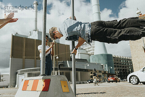 Athletic young man doing flag figure on pole at street